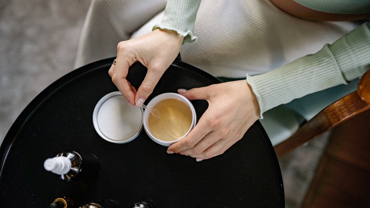 A close-up of hands opening a skincare container with beauty products on a black table.